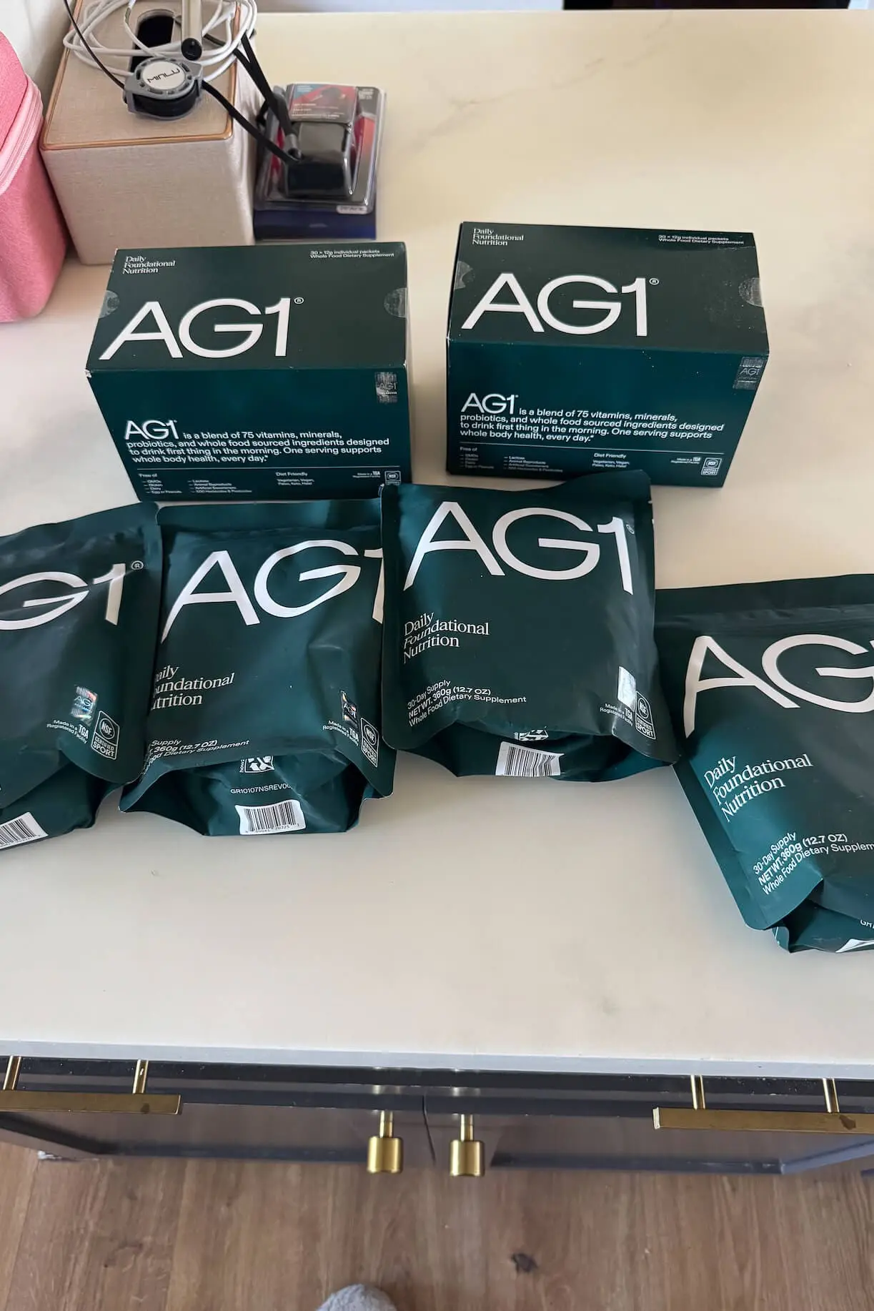 Collection of AG1 Daily Foundational Nutrition packets and boxes displayed on a kitchen counter, showing a stocked-up supplement supply.